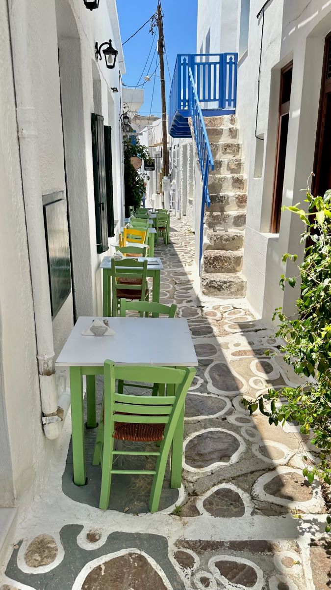 Sage green and white cafe tables and chairs set out down a narrow whitewashed street