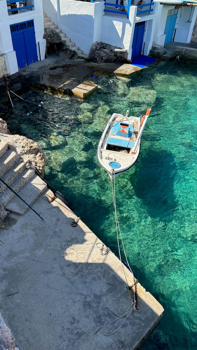 Rowing boat floating on clear turquoise sea beside traditional settlements at the water's edge