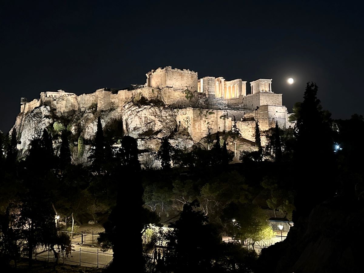 Parthenon lit up at night with the full moon behind